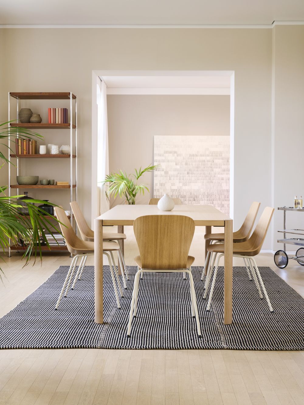 Moderner Essbereich mit Holztisch, vier Stühlen, Teppich und Zimmerpflanzen in einem hellen Raum.