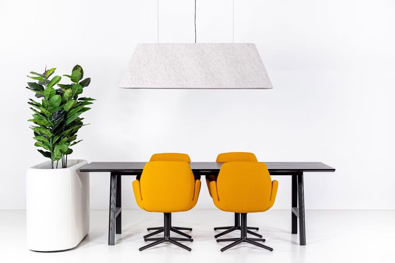 Moderner Konferenztisch mit vier gelben ergonomischen Stühlen und Topfpflanze, stilvolle Beleuchtung darüber.