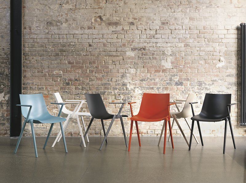 Sechs bunte, ergonomische Stühle vor einer Ziegelwand bieten stilvolle Sitzlösungen für Büro oder Zuhause.