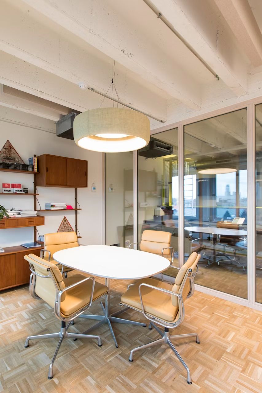 Moderner Besprechungsraum mit ovalem Tisch, ergonomischen Stühlen und großer Hängelampe in einer Glaswandumgebung.