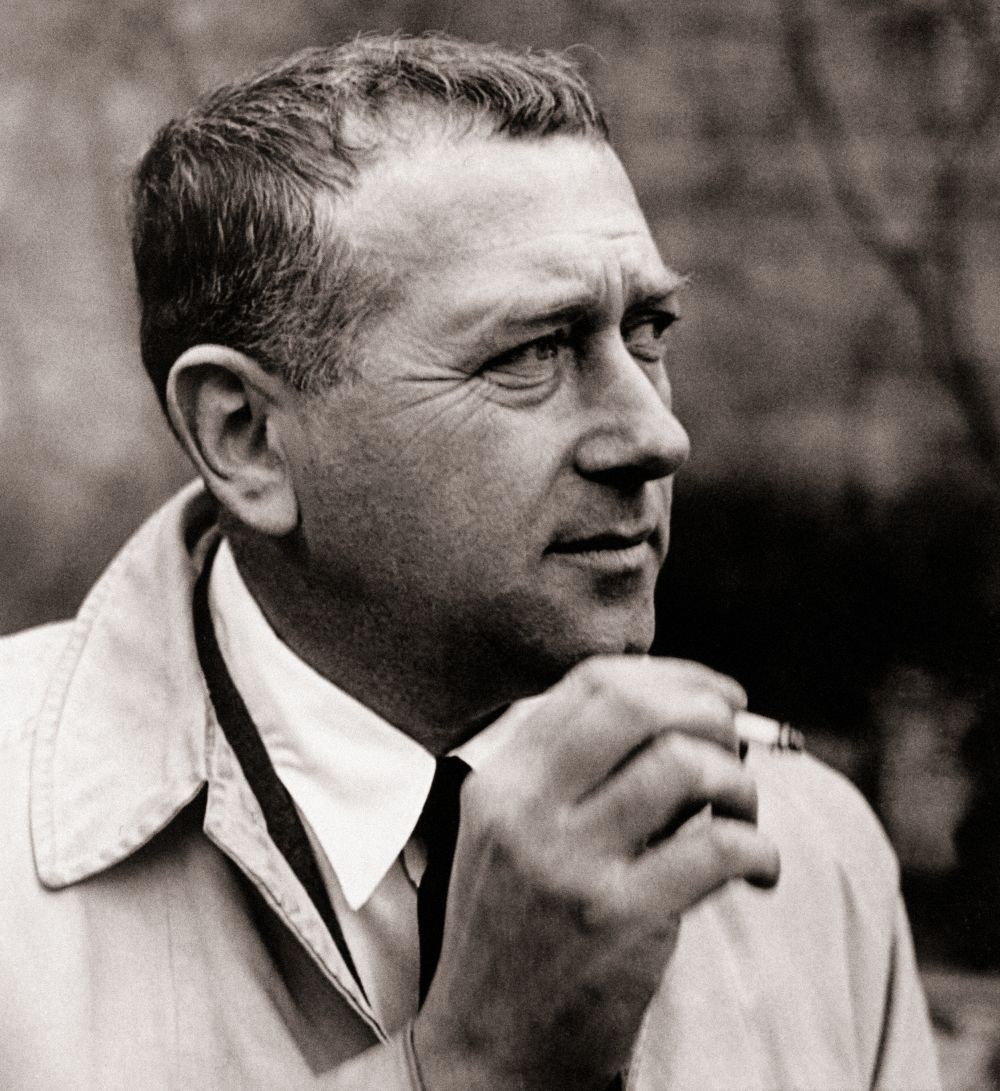 Schwarzweißfoto eines Mannes in einem Mantel, der eine Zigarette hält; nachdenklicher Ausdruck.