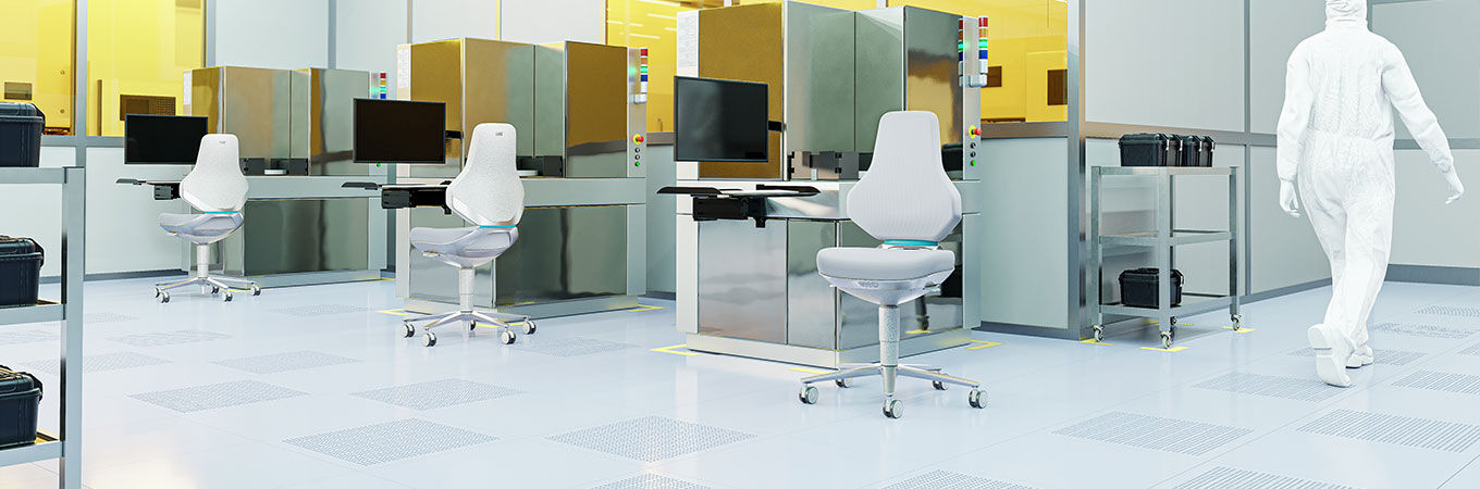 Laborpersonal in blauen Schutzanzügen arbeitet an High-Tech-Geräten und verwendet ergonomische Stühle.