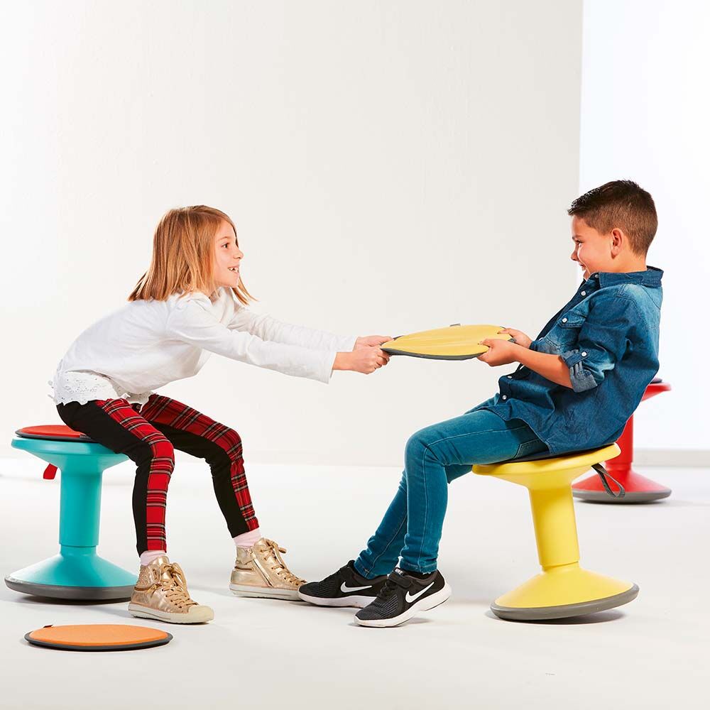Zwei lachende Kinder spielen mit ergonomischen Hockern in verschiedenen Farben, fördern aktives und dynamisches Sitzen.