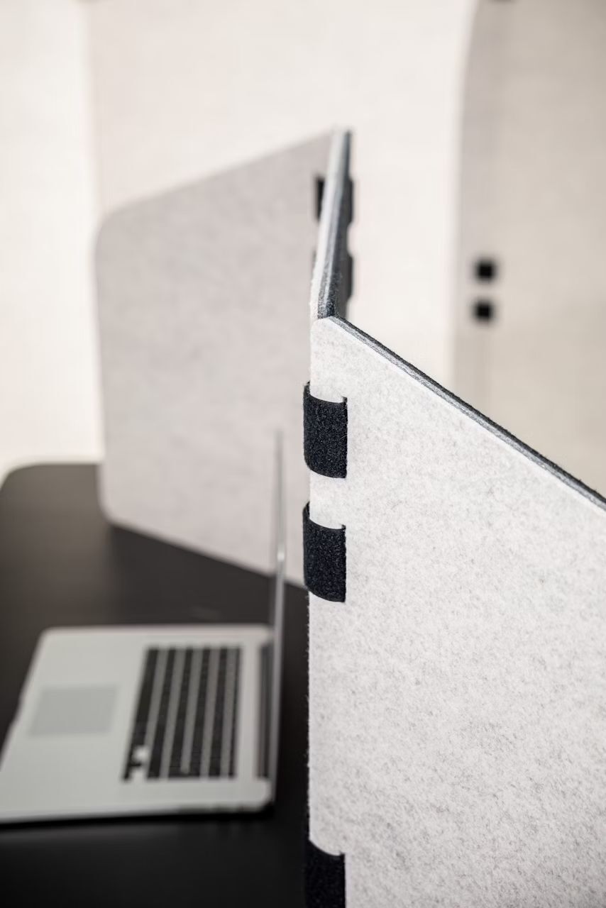 Ergonomische Schreibtischtrennwand neben einem Laptop, ideal für konzentriertes Arbeiten und Privatsphäre im Büro.