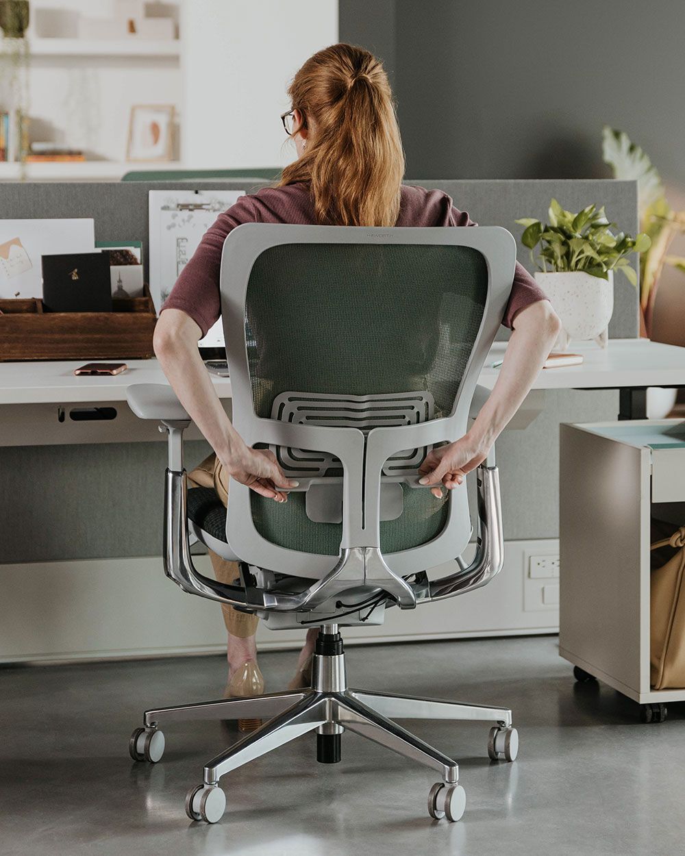 Frau passt ergonomischen Bürostuhl im modernen Büro an, um dynamisches Sitzen zu fördern.