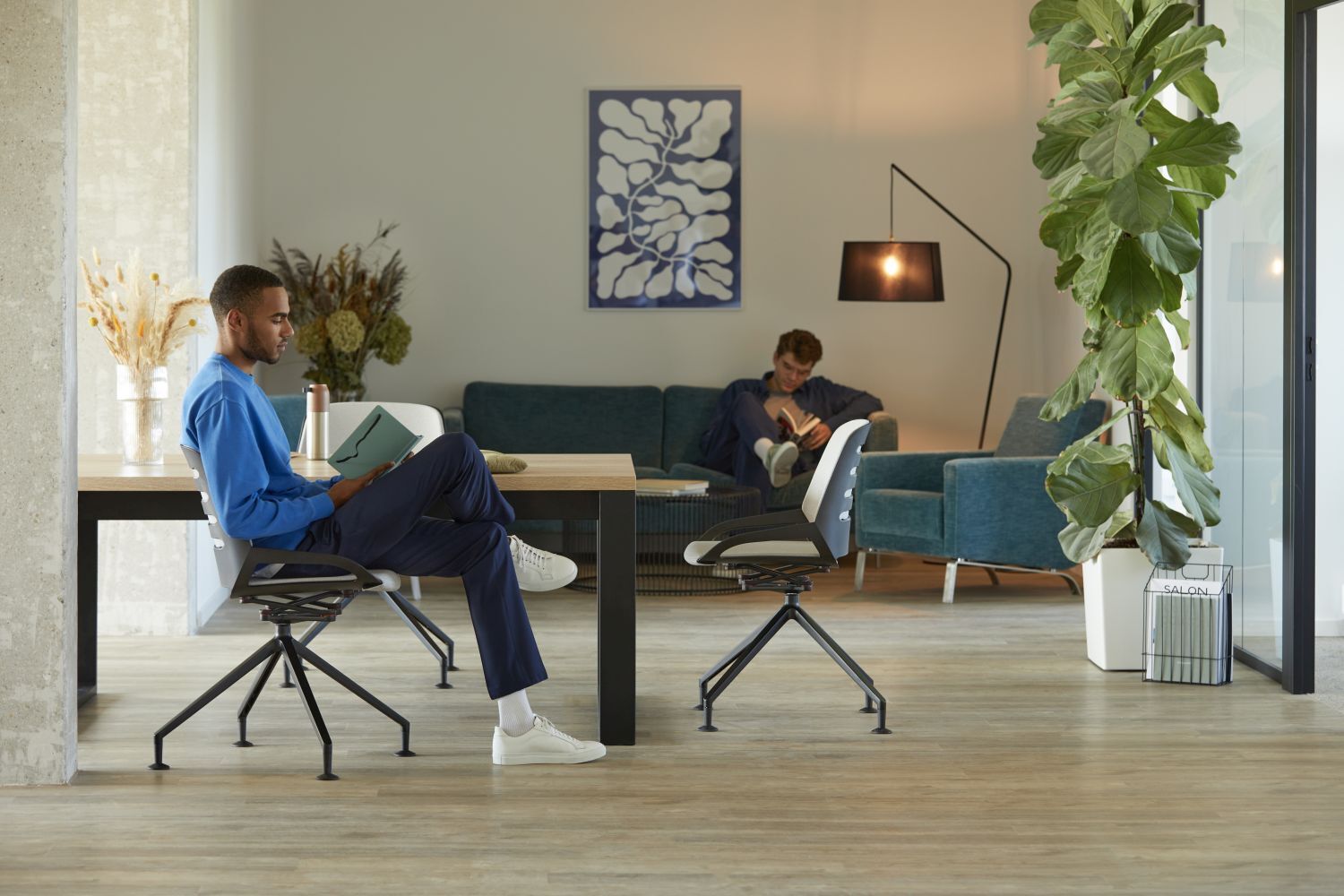 Zwei Männer entspannen in einem modernen Büro mit ergonomischen Stühlen und Pflanzen, helle, angenehme Atmosphäre.