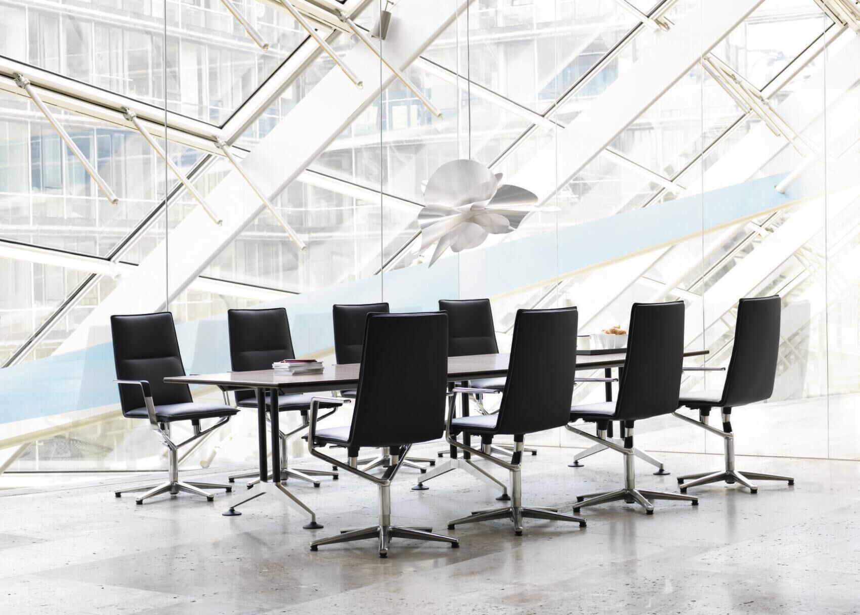 Eleganter Konferenzraum mit acht ergonomischen Drehstühlen um einen modernen Tisch vor einer Glasfassade.