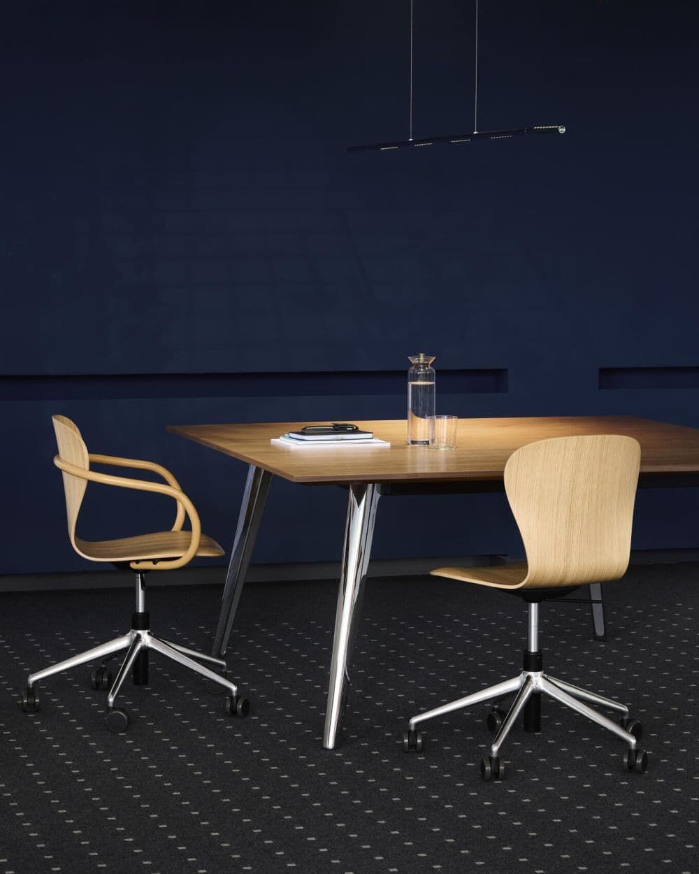 Zwei ergonomische Bürostühle an einem eleganten Holztisch, beleuchtet von einer modernen Hängelampe.