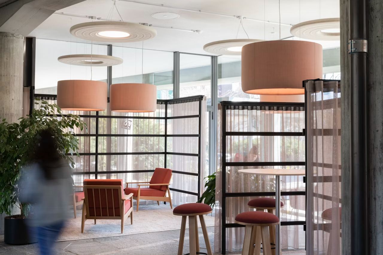 Modernes Büro mit roten Stühlen und großen Deckenleuchten, umgeben von Raumteilern und Pflanzen.