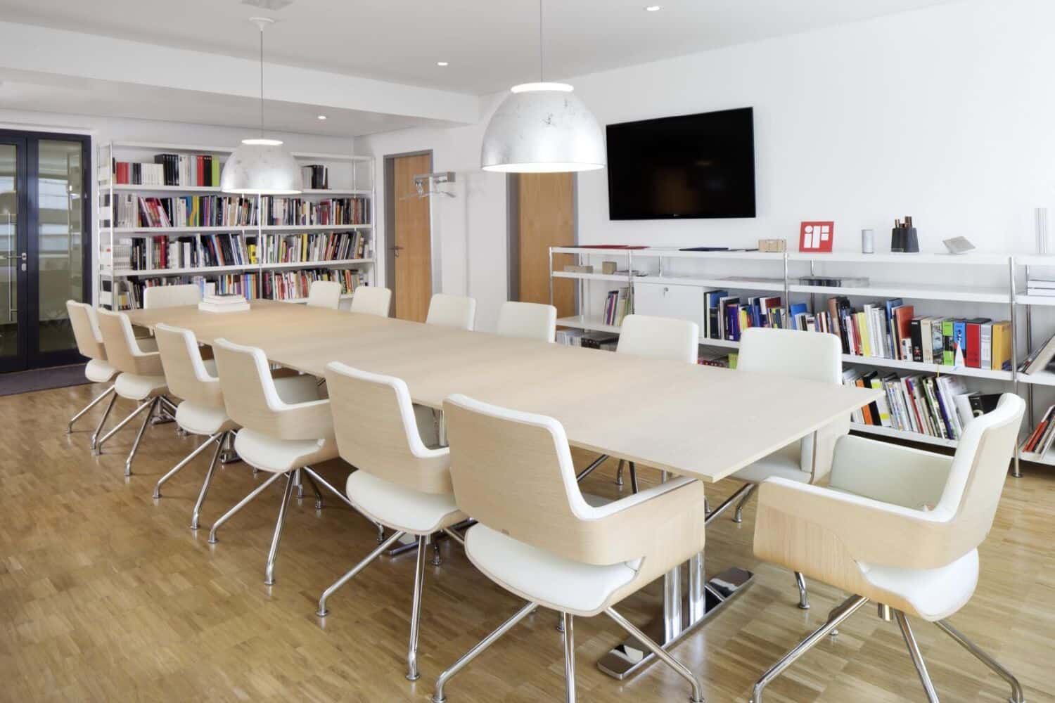Moderner Konferenzraum mit ergonomischen Stühlen, einem langen Tisch und Bücherregalen im Hintergrund.