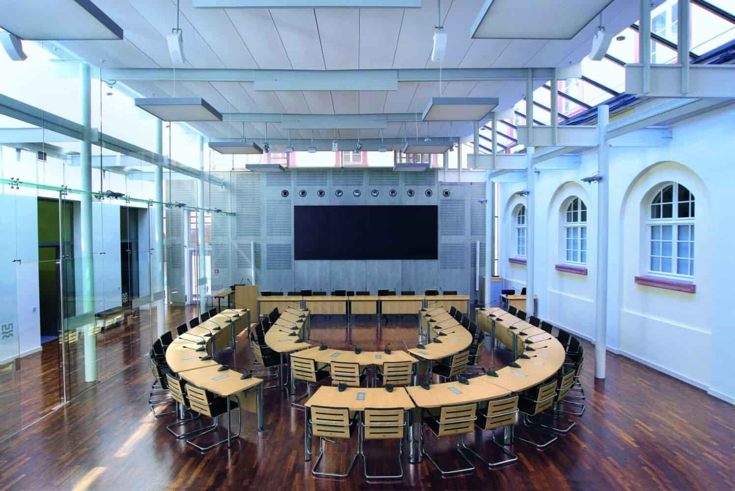 Moderner Konferenzraum mit U-förmigen Tischen und ergonomischen Stühlen, helle Glasarchitektur.