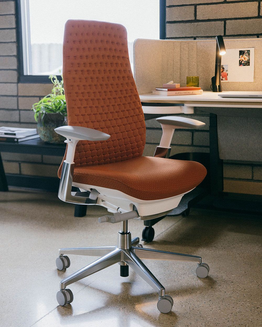 Ergonomischer Bürostuhl in Orange mit verstellbaren Armlehnen und drehbarem Metallfuß, geeignet für dynamisches Sitzen.