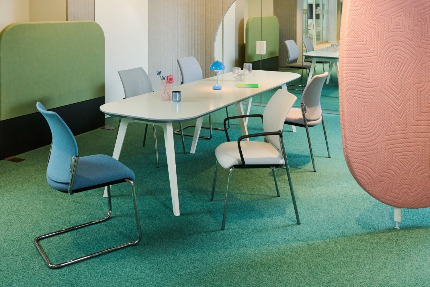 Moderner Besprechungsraum mit ergonomischen Stühlen, weißem Tisch und bunter Akustiktrennwand, betont dynamische Büroeinrichtung.