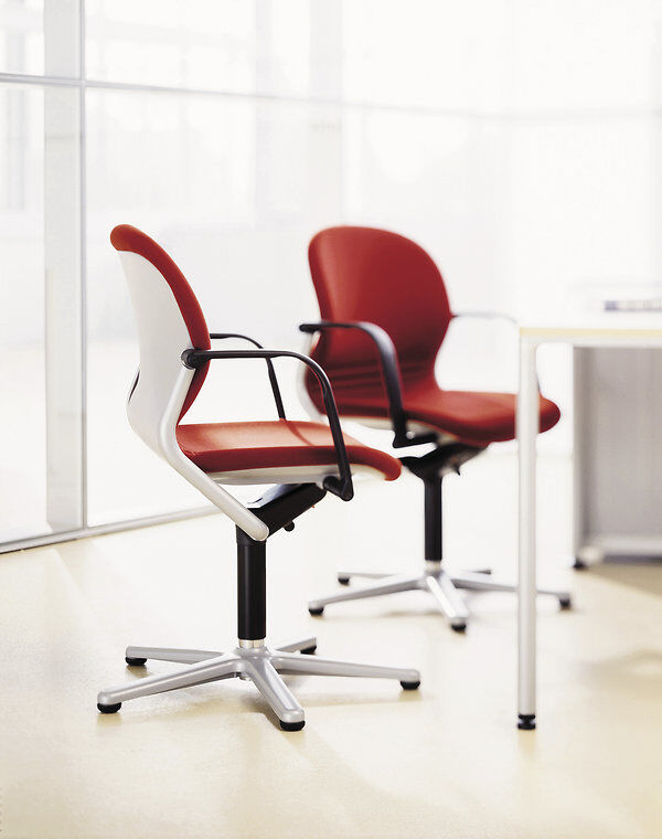 Zwei rote ergonomische Bürostühle stehen in einem hellen Raum neben einem Tisch.