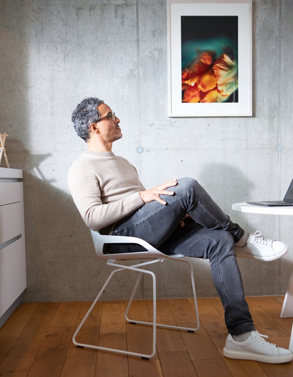 Mann sitzt bequem auf ergonomischem Stuhl in modernem Büro, Betonwand mit Kunstbild im Hintergrund.