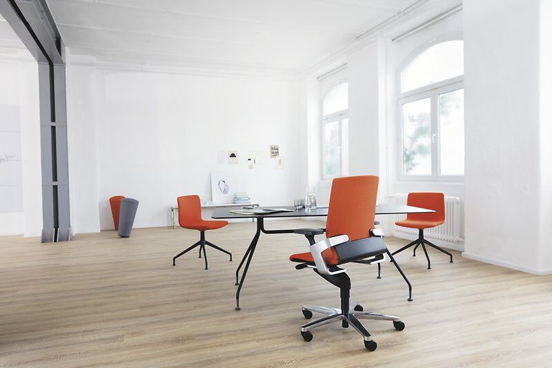 Helle Büroumgebung mit modernen, orangefarbenen ergonomischen Stühlen und einem großen, runden Tisch in der Mitte.