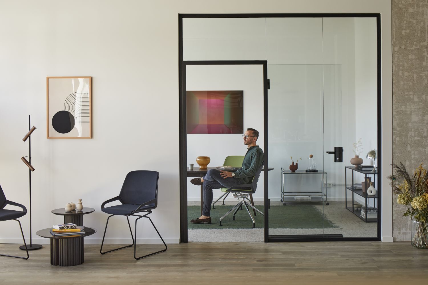 Mann sitzt auf ergonomischem Bürostuhl in modernem Büro mit Glaswänden und stilvollen Möbeln.