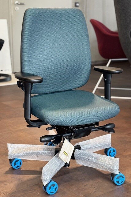 Ergonomischer Bürostuhl mit blauer Polsterung und verstellbaren Armlehnen auf einer Ausstellungsfläche.