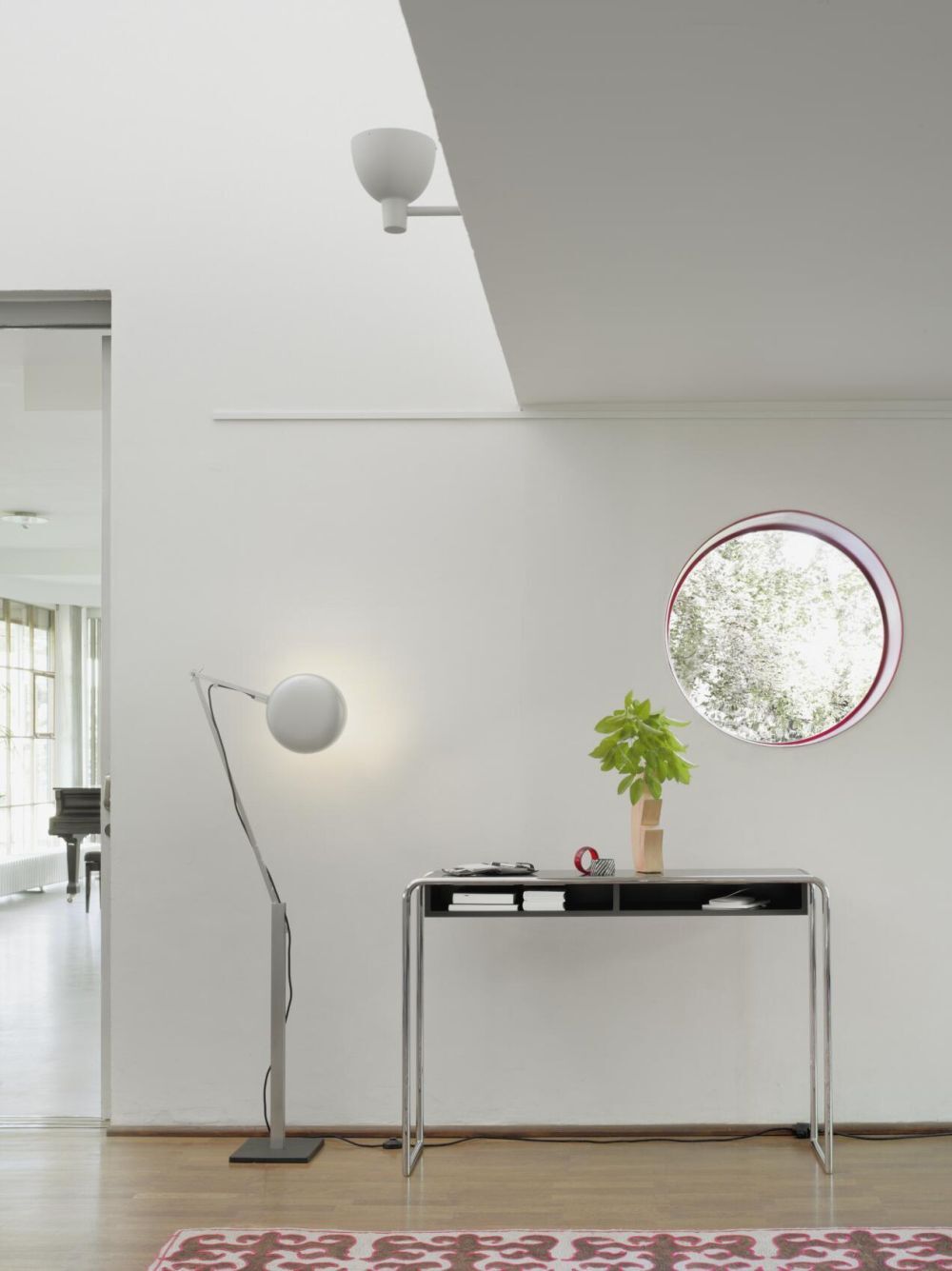 Moderner Schreibtisch mit Lampe und Pflanze, minimalistisches Design, rundes Fenster im Hintergrund.