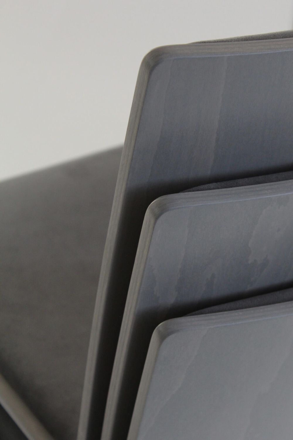 Nahaufnahme von gestapelten grauen Holzstühlen mit glatten, abgerundeten Kanten und minimalistischem Design.