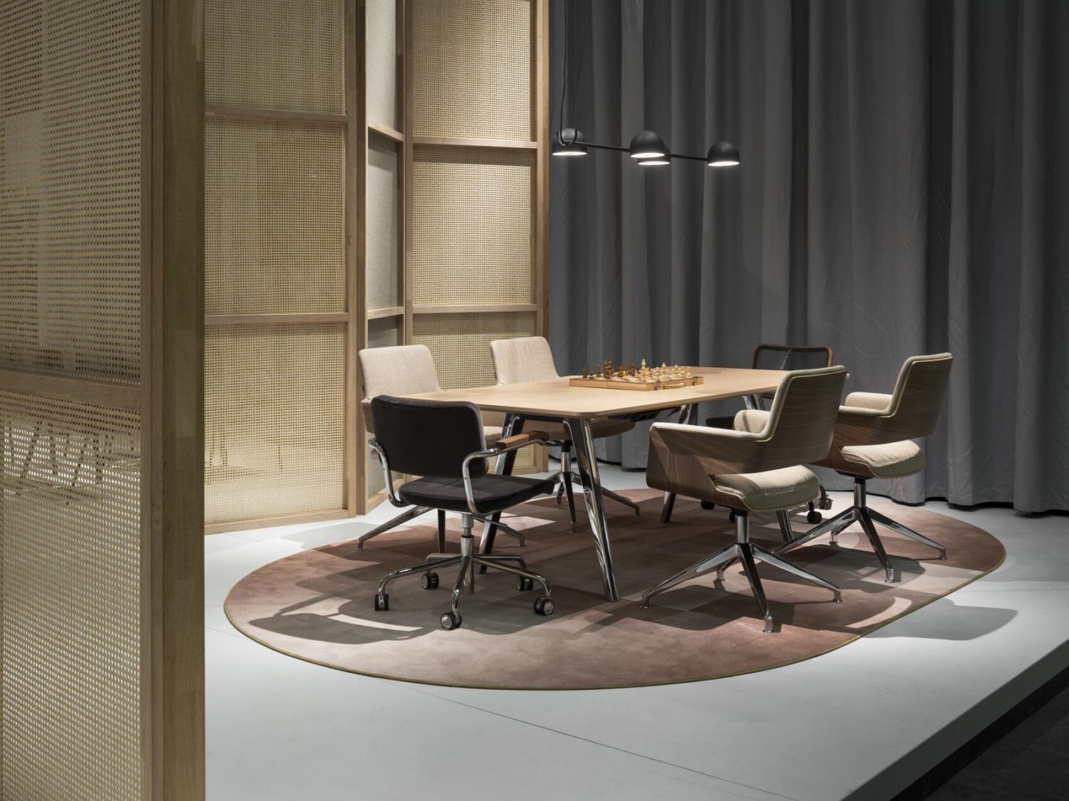 Moderner Konferenztisch mit sechs ergonomischen Stühlen auf Teppich, beleuchtet von Hängelampen.