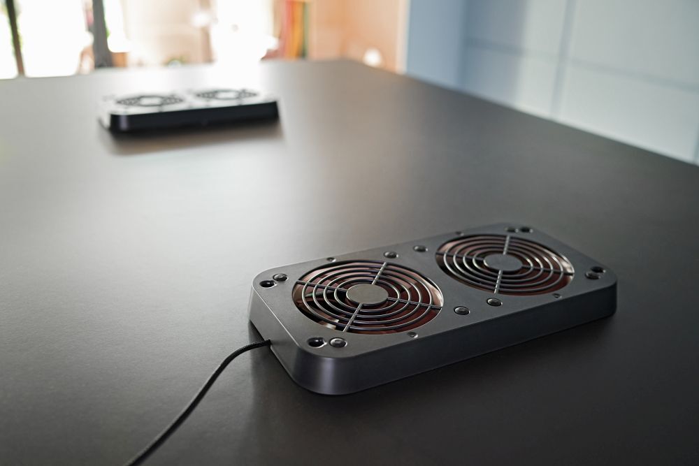 Zwei schwarze Tischventilatoren auf einer dunklen Oberfläche, fokussiert auf den vorderen Ventilator.