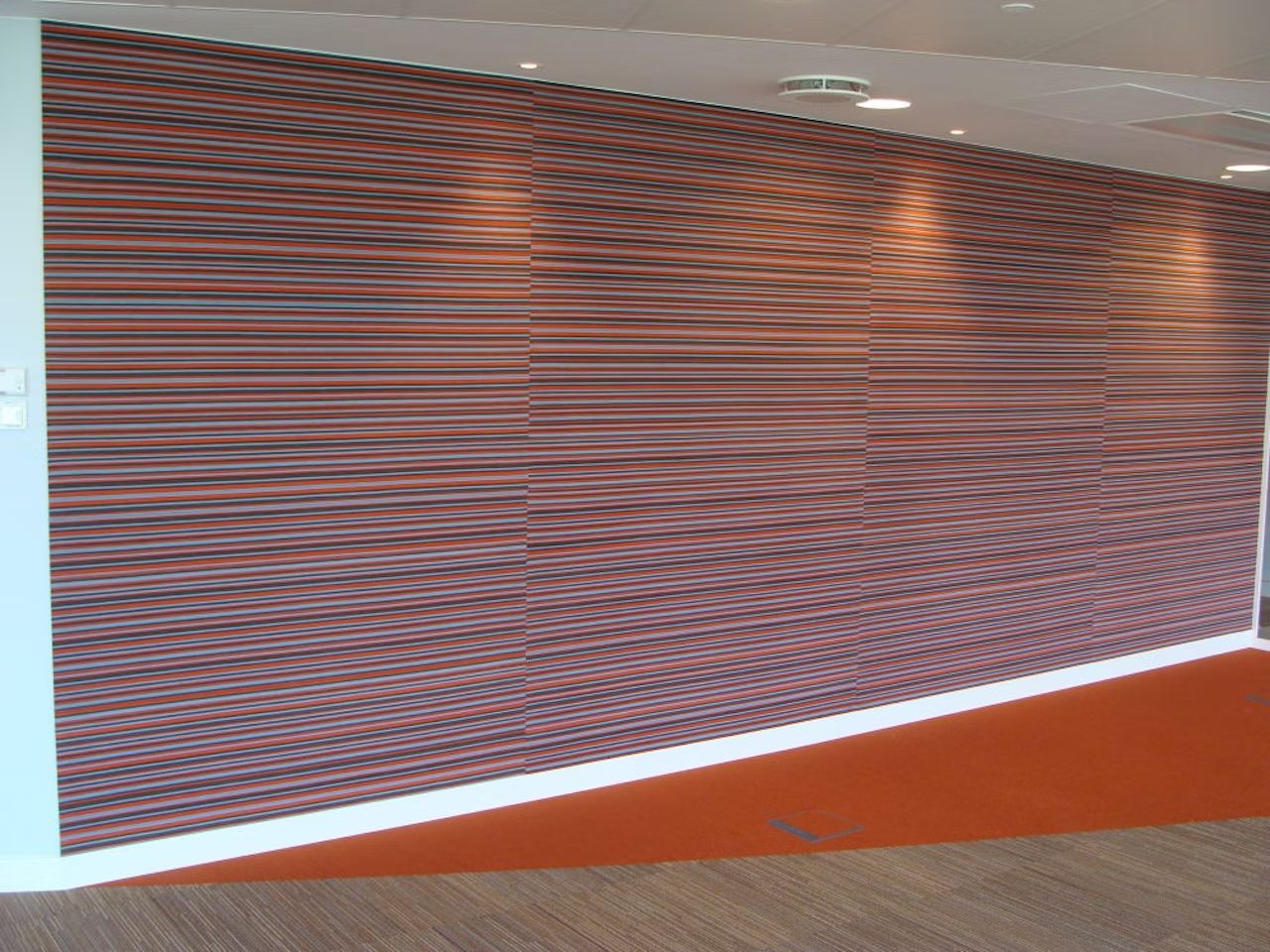 Moderne Wand mit horizontalen, bunten Streifen in einem Bürobereich, betont durch dezente Beleuchtung.