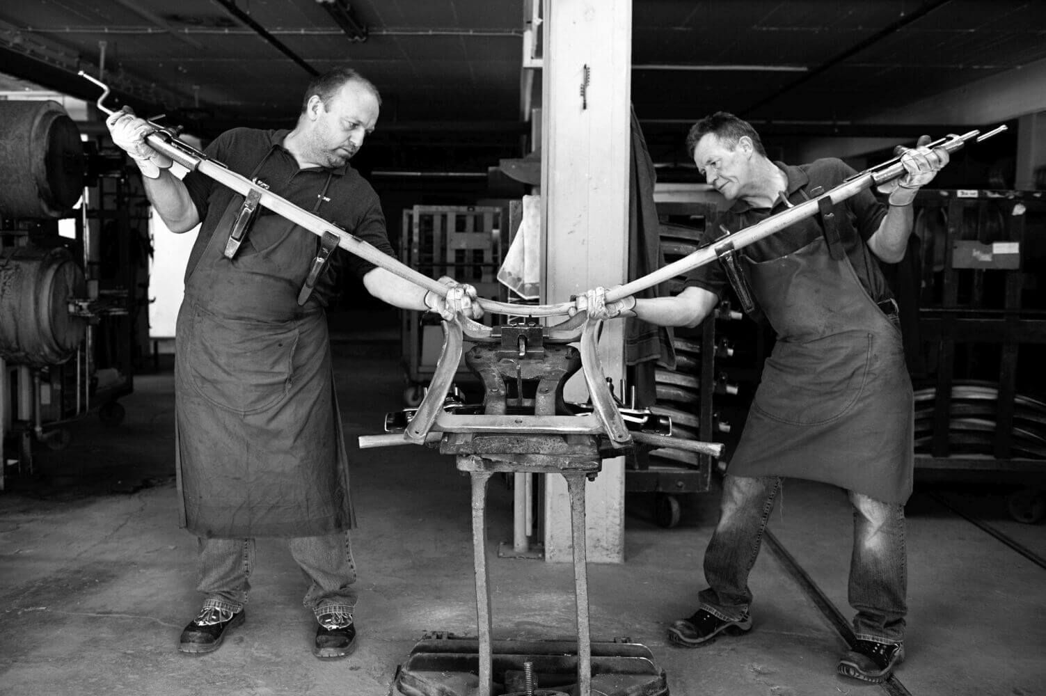 Zwei Handwerker fertigen in einer Fabrik ergonomische Stuhlgestelle von Hand an.