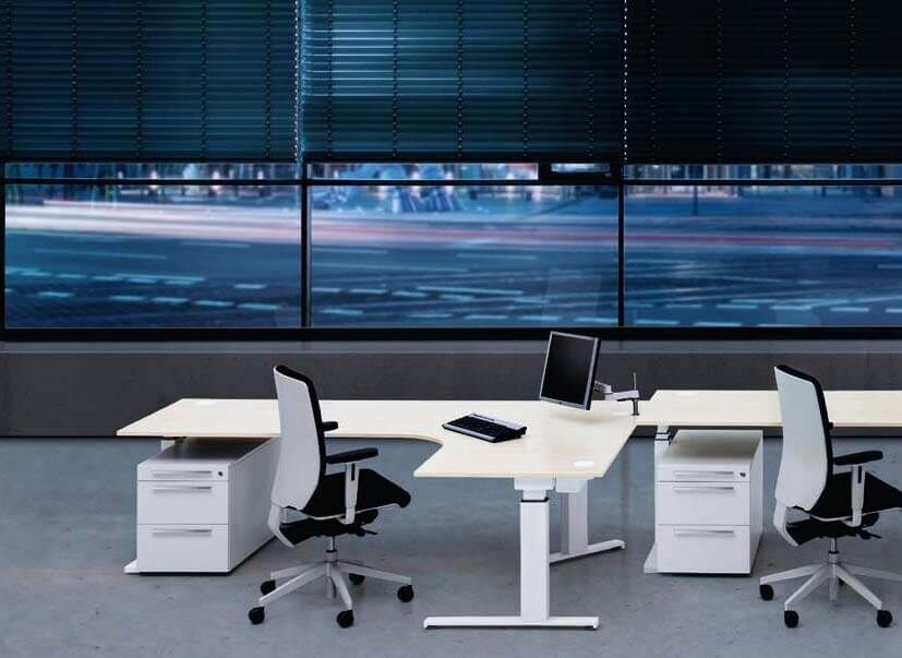 Moderne Büroumgebung mit ergonomischen Stühlen und höhenverstellbaren Schreibtischen vor großen Fenstern.