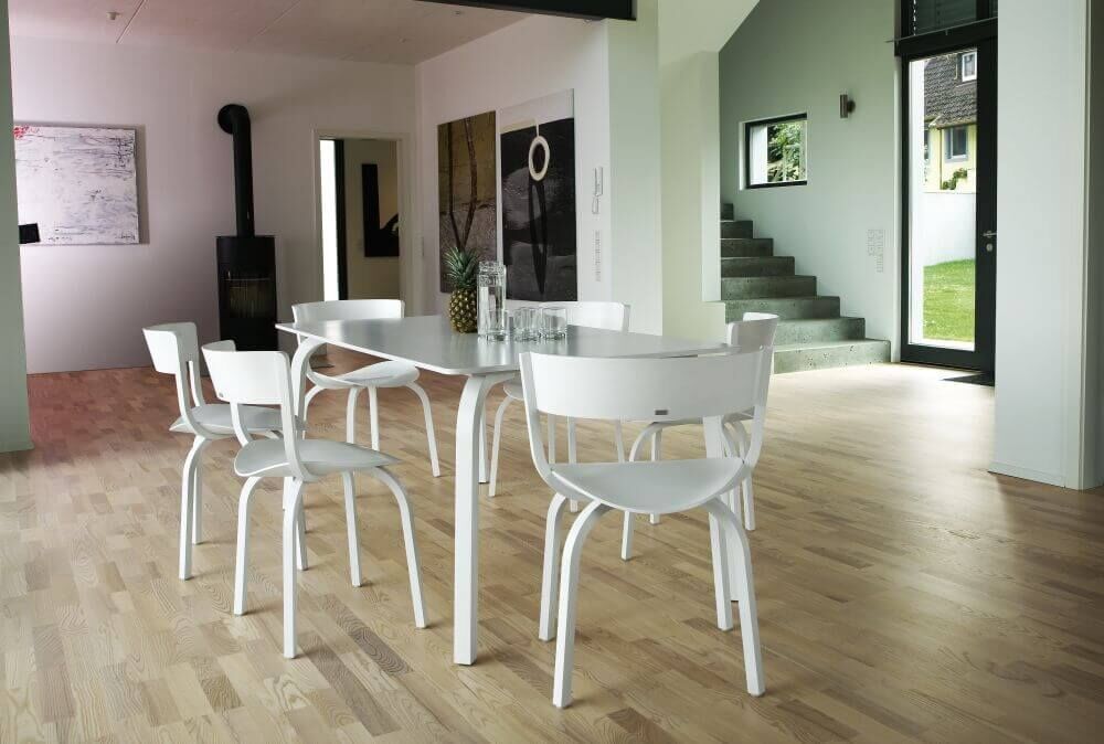Moderner Essbereich mit weißen Stühlen und Tisch auf Holzfußboden, helle und minimalistische Einrichtung.