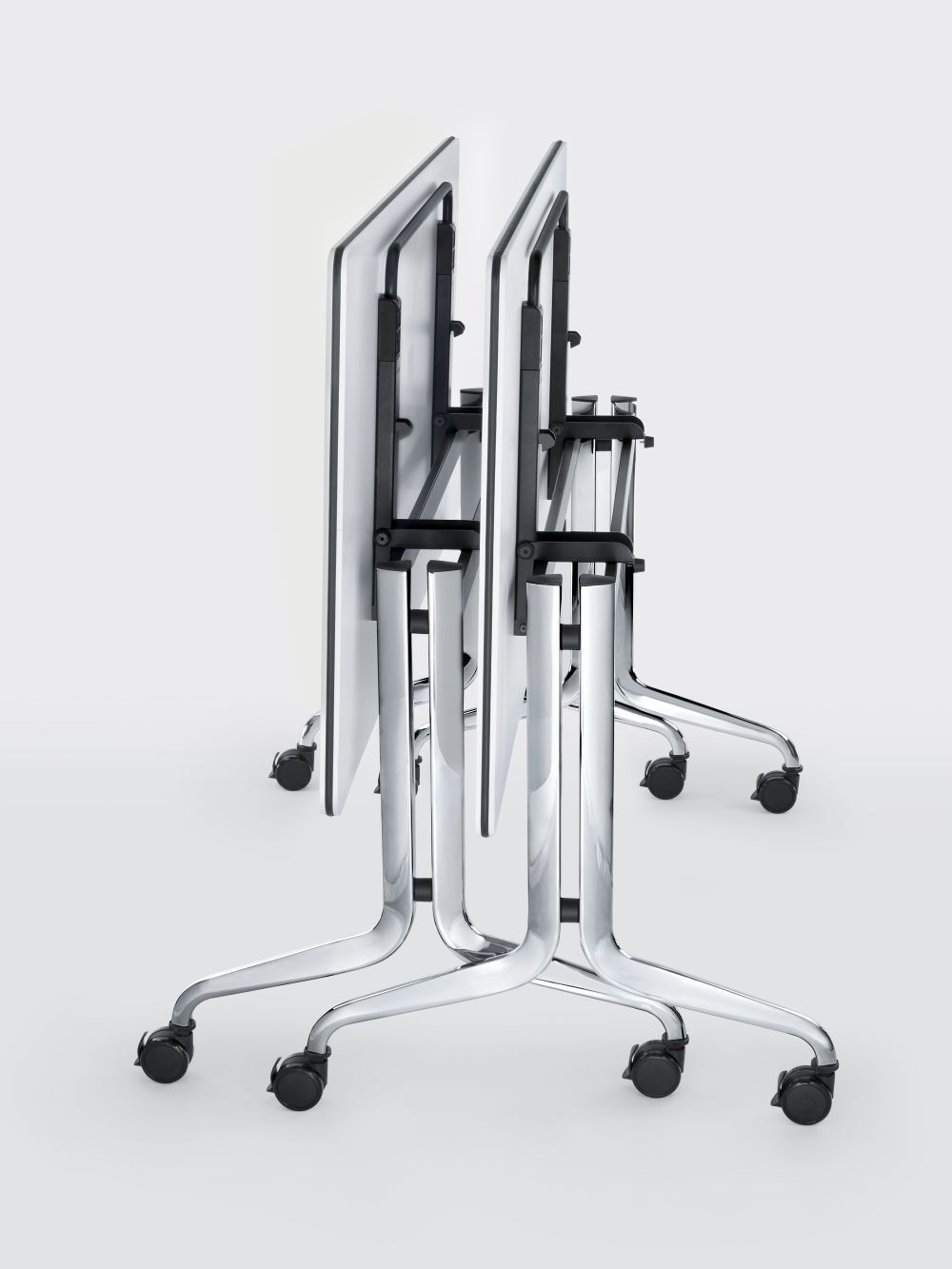 Gestapelte Bürotische mit klappbaren Platten und Rollen, ideal für flexible Arbeitsumgebungen.