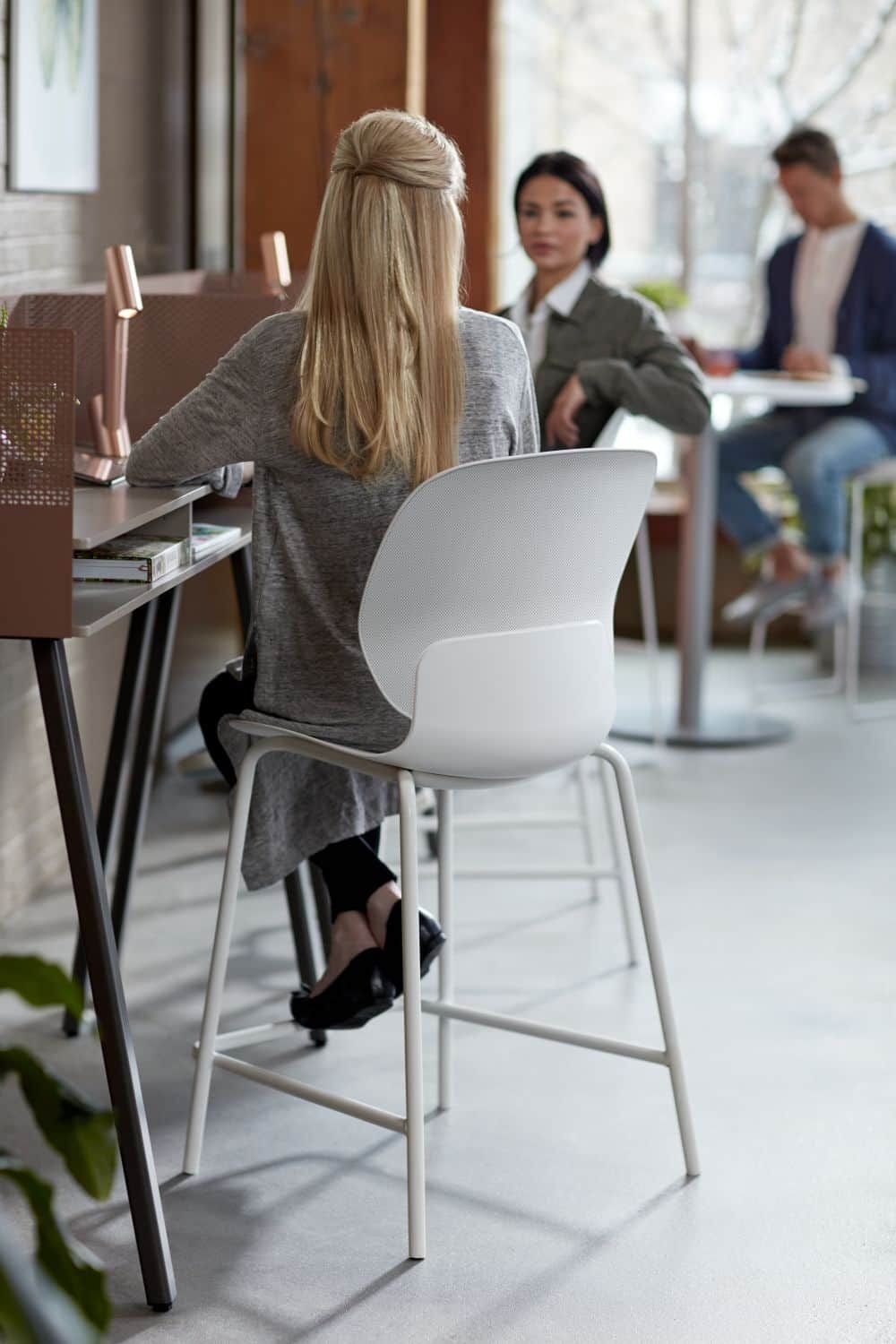 Drei Personen in einem modernen Büro, die ergonomische Stühle beim Gespräch verwenden. Helle, entspannte Atmosphäre.