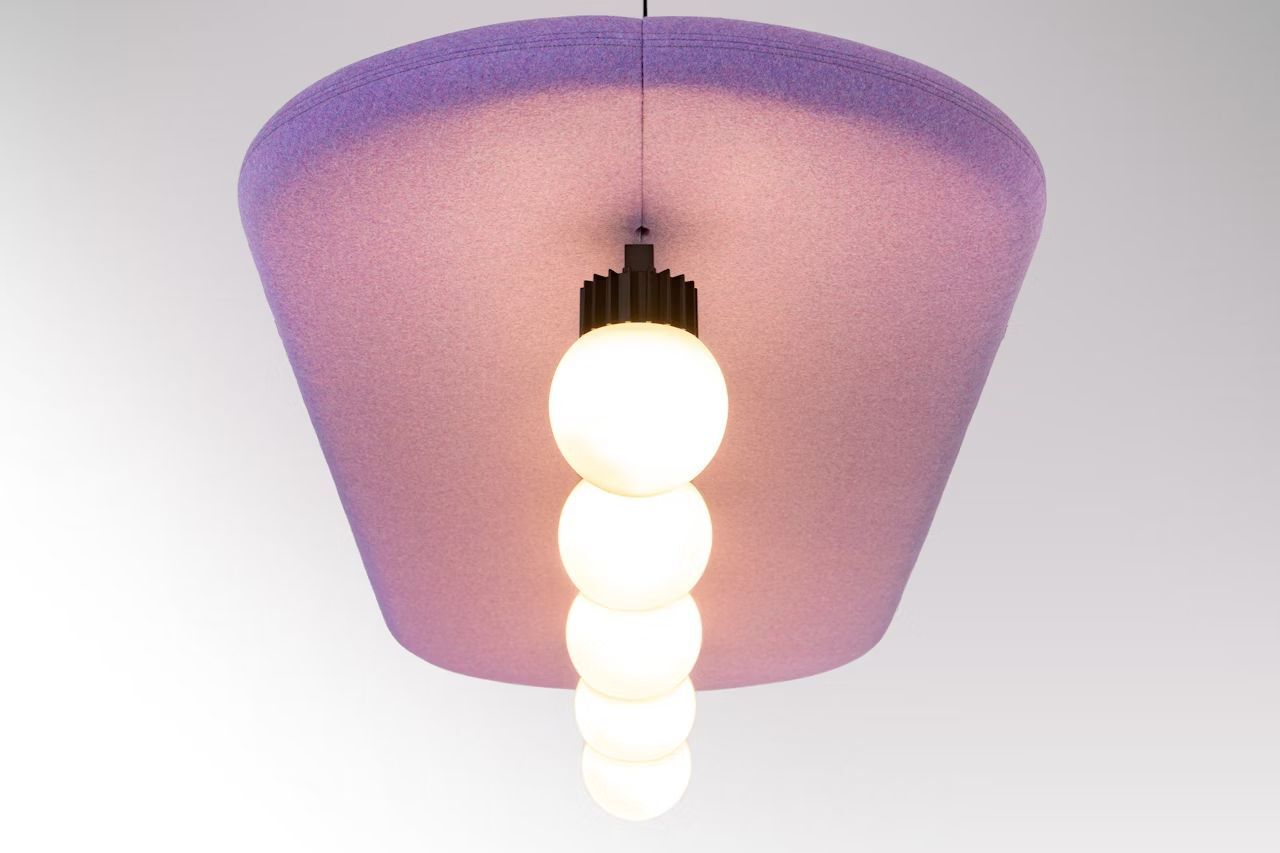 Hängelampe mit fünf leuchtenden Kugeln, montiert an einer pink-violetten Akustikdecke.
