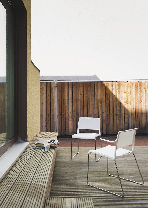 Zwei weiße Designstühle auf einer Terrasse mit Holzzaun. Modernes, minimalistisches Ambiente für den Außenbereich.