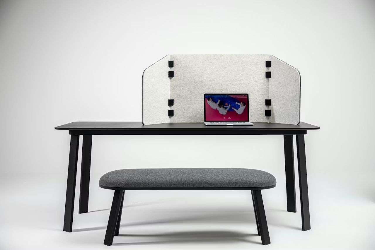Schreibtisch mit Sichtschutz, Laptop und Bank, geeignet für ergonomisches Arbeiten im Homeoffice.
