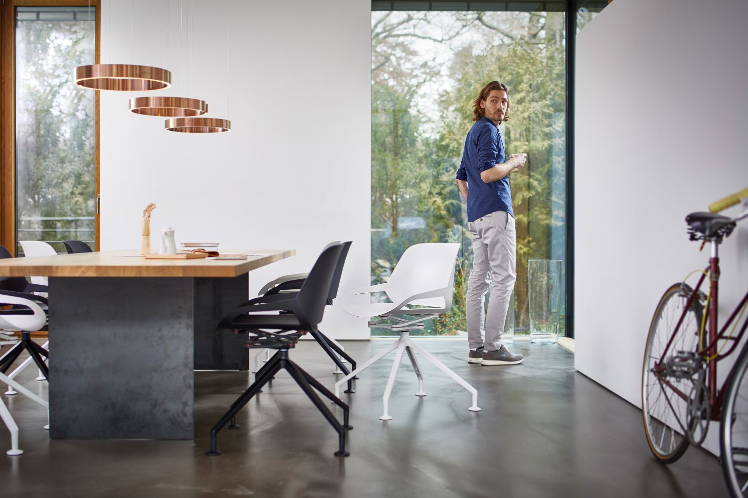 Mann in modernem Büro mit ergonomischen Stühlen, neben einem Tisch und einem Fahrrad, blickt aus dem Fenster.