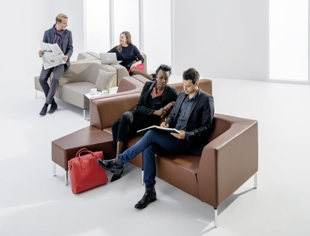 Personen sitzen auf stilvollen Sofas, arbeiten und entspannen sich in moderner Büroatmosphäre.