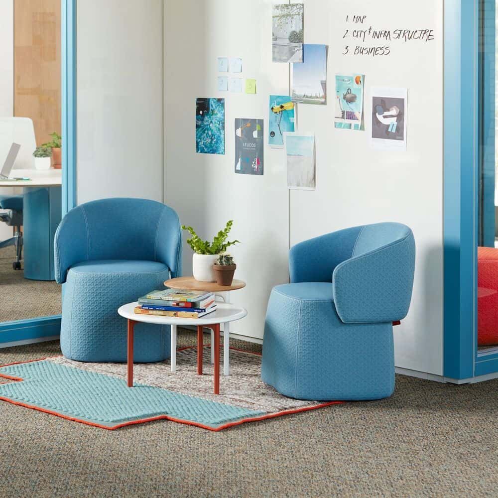 Zwei blaue, ergonomische Stühle um einen runden Tisch mit Pflanzen und Büchern, vor einer Wand mit Notizen.