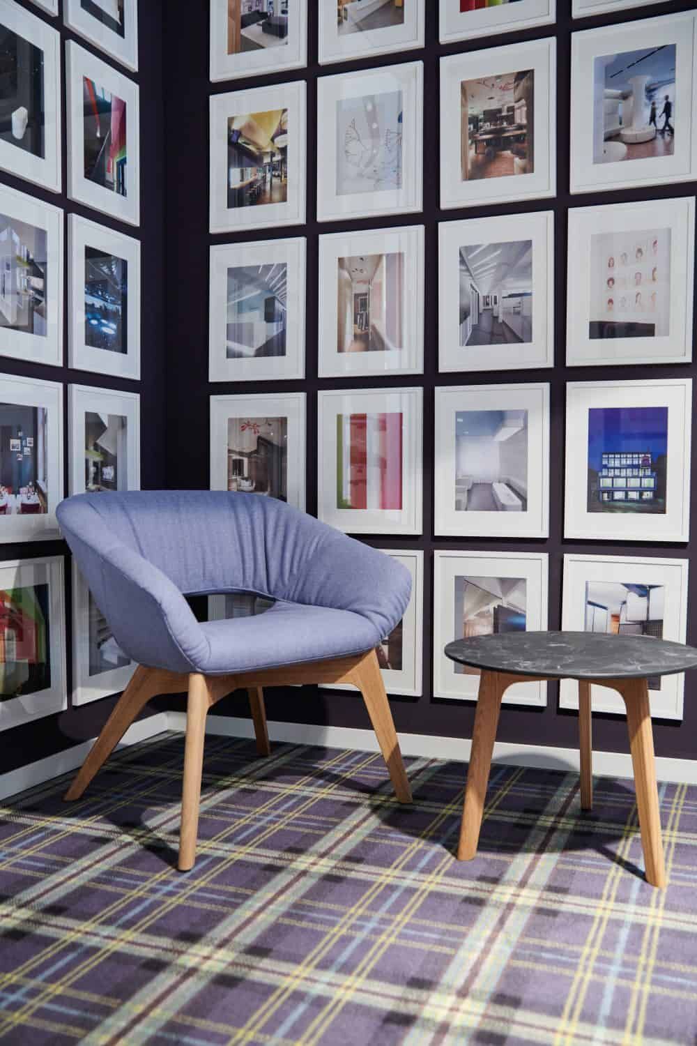 Moderner blauer Sessel mit Holztisch vor einer Galerie-Wand mit gerahmten Bildern auf kariertem Teppich.