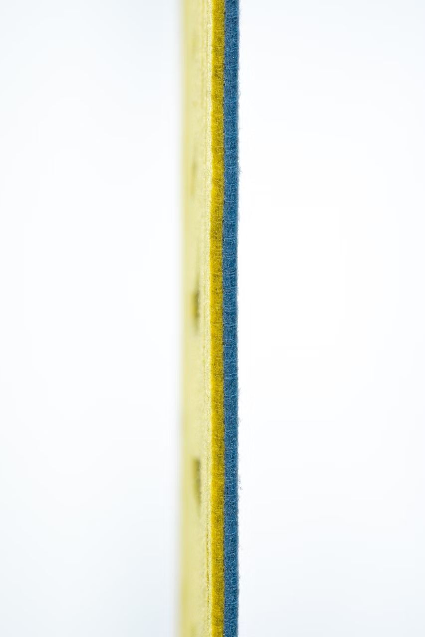 Nahaufnahme der Kante eines gelben, blauen und grauen Plattenmaterials auf weißem Hintergrund.