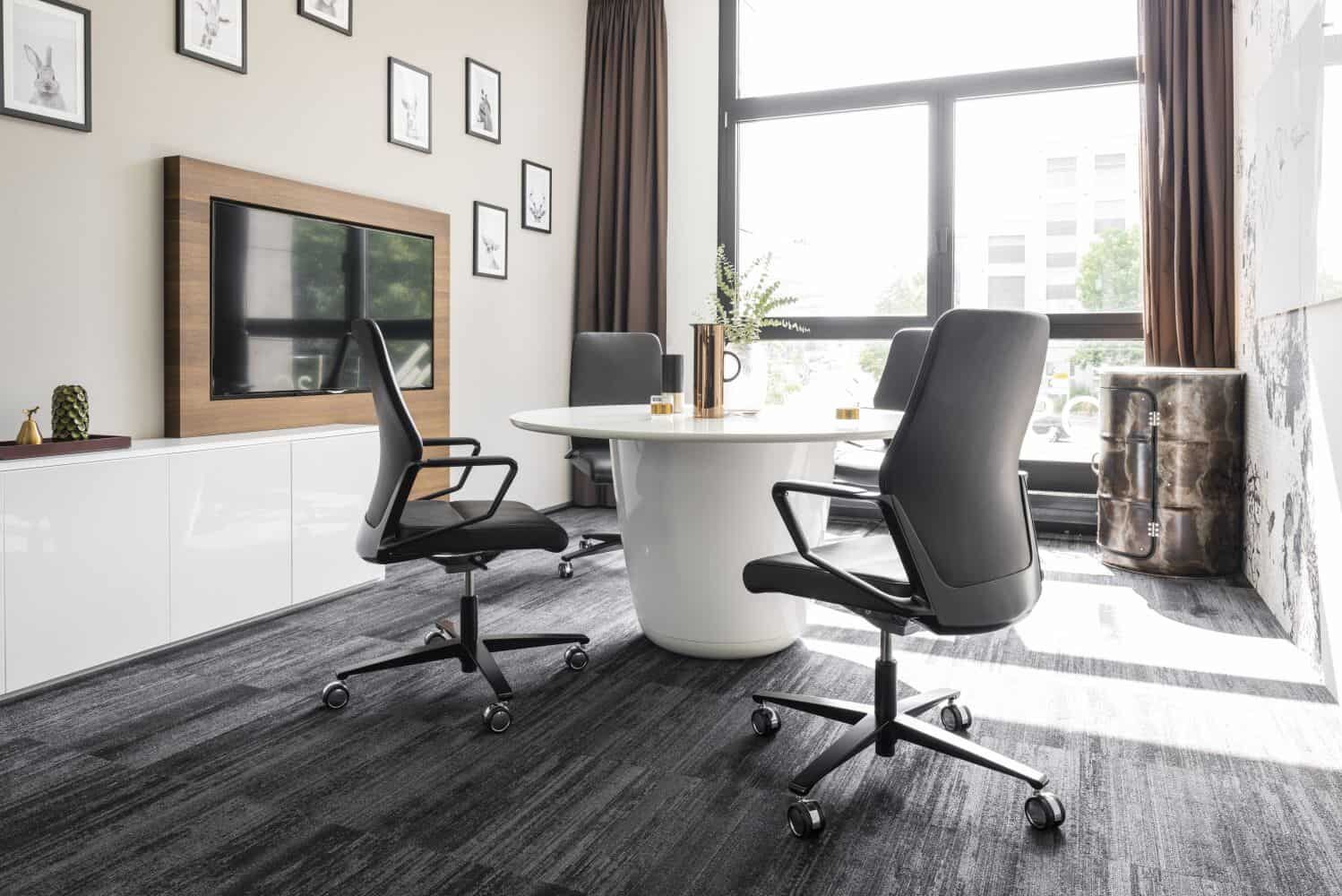 Moderne Besprechungsecke mit ergonomischen Bürostühlen und rundem Tisch, ideal für gesundes Sitzen im Büro.