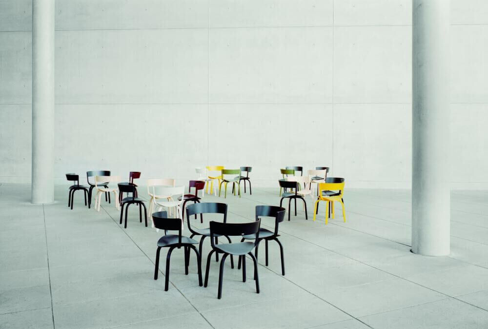 Mehrere bunte Stühle und Tische in einem modernen, minimalistisch gestalteten Raum mit Betonwänden.