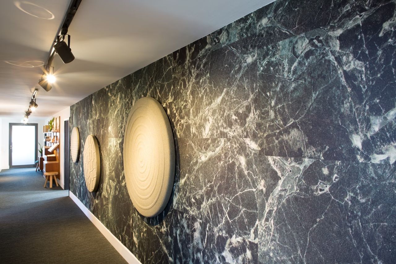 Flur mit grauer Marmorwand und kreisförmigen Akustikpaneelen, moderne Büroeinrichtung im Hintergrund sichtbar.