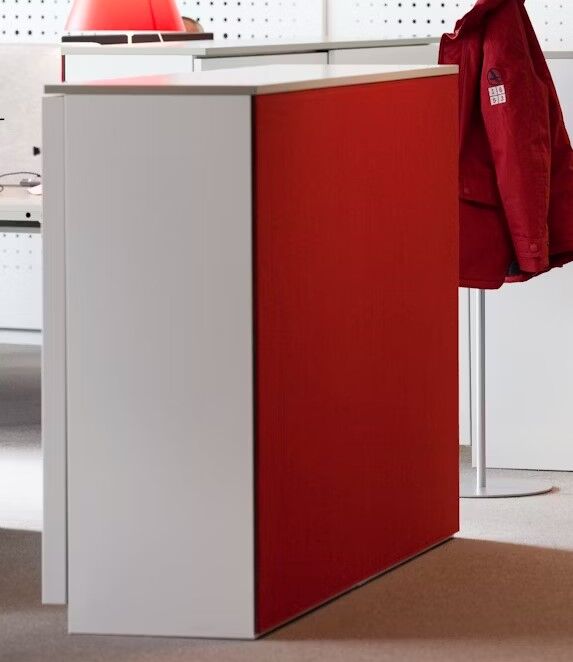 Bürokabine mit weißen Wänden und roter Vorderseite. Rote Jacke hängt an der Rückseite des Stuhls.