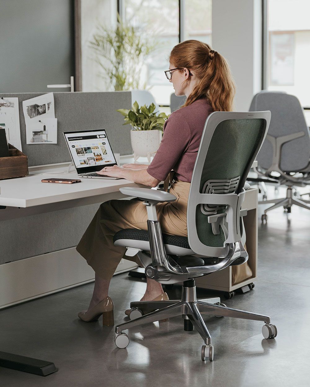 Frau sitzt in einem ergonomischen Bürostuhl am Schreibtisch und arbeitet am Laptop.