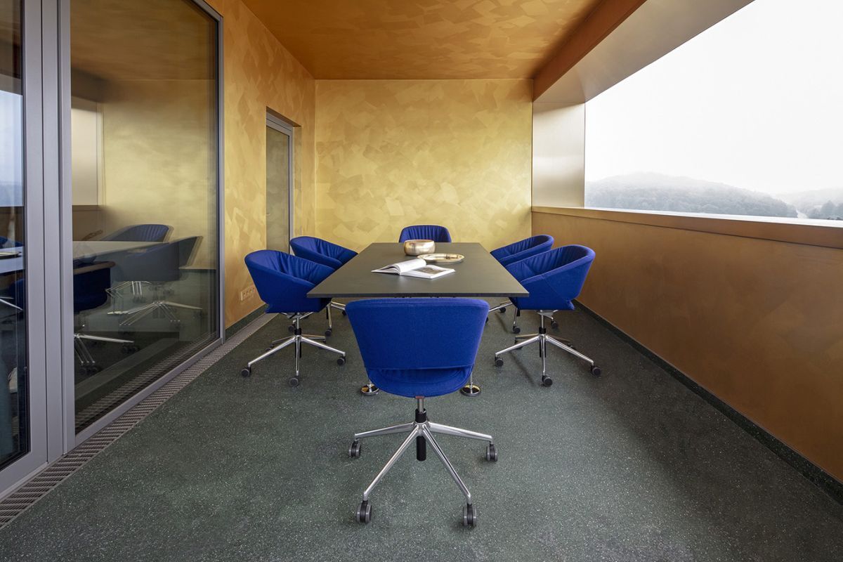 Moderner Konferenzraum mit blauen ergonomischen Stühlen um einen schwarzen Tisch, große Fenster mit Aussicht.