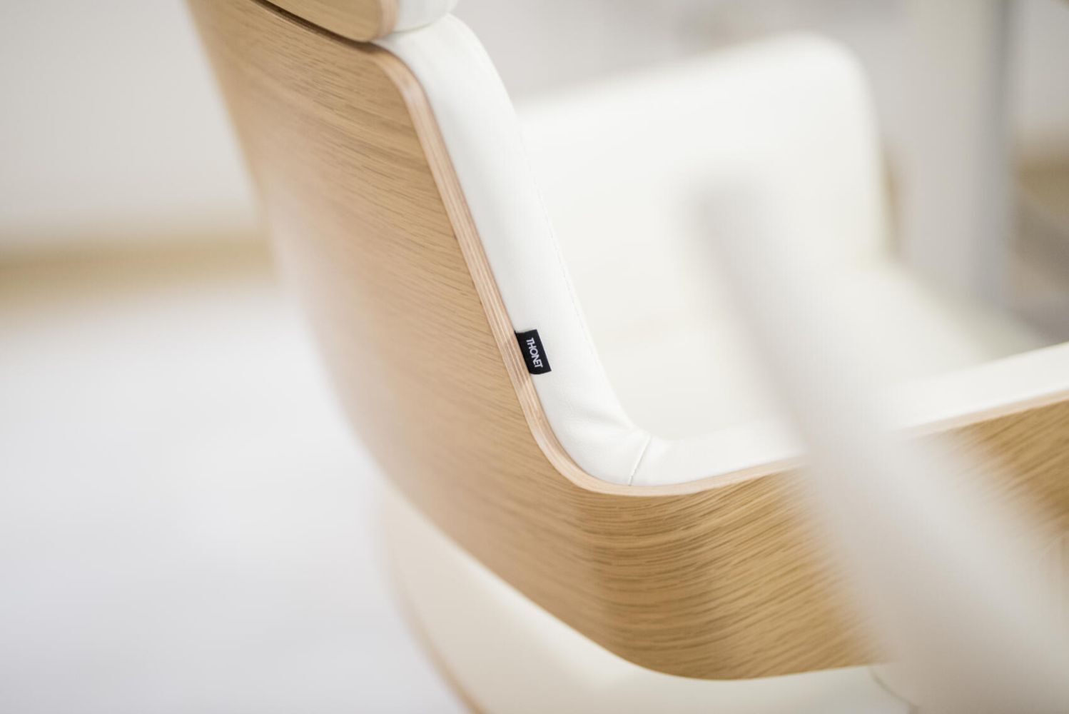 Nahaufnahme eines eleganten Bürostuhls mit Holzverkleidung und heller Polsterung, betont ergonomisches Design.
