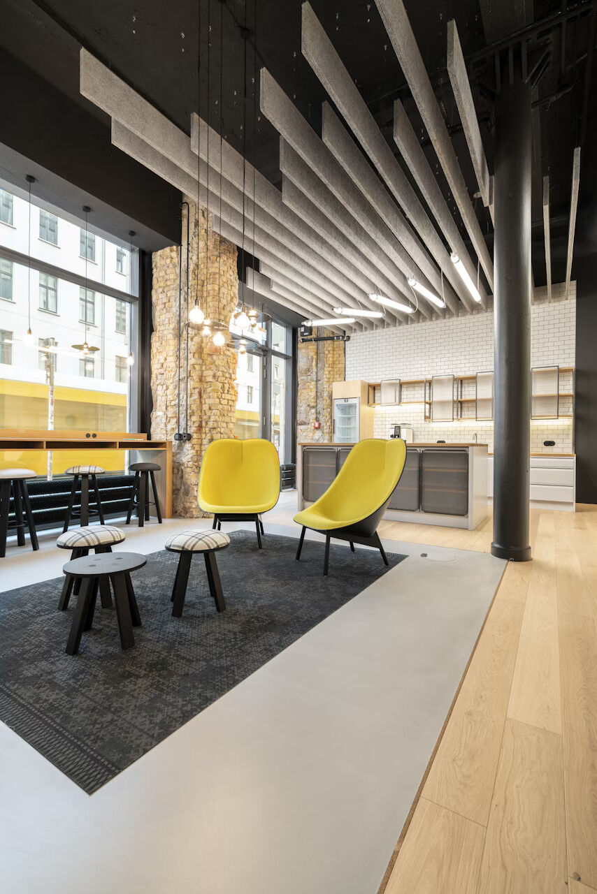 Modernes Büro mit gelben Stühlen, schwarzen Hockern, industriellem Dekor und Holz- sowie Steinelementen im Innenraum.