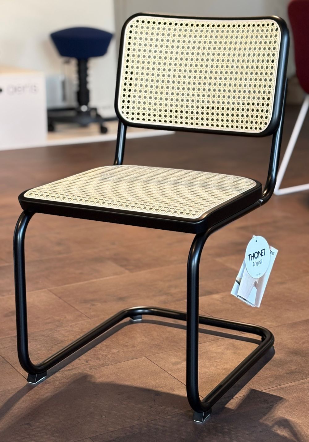 Klassischer Stuhl mit schwarzem Metallrahmen und geflochtener Sitzfläche, auf einem stilvollen Holzboden.