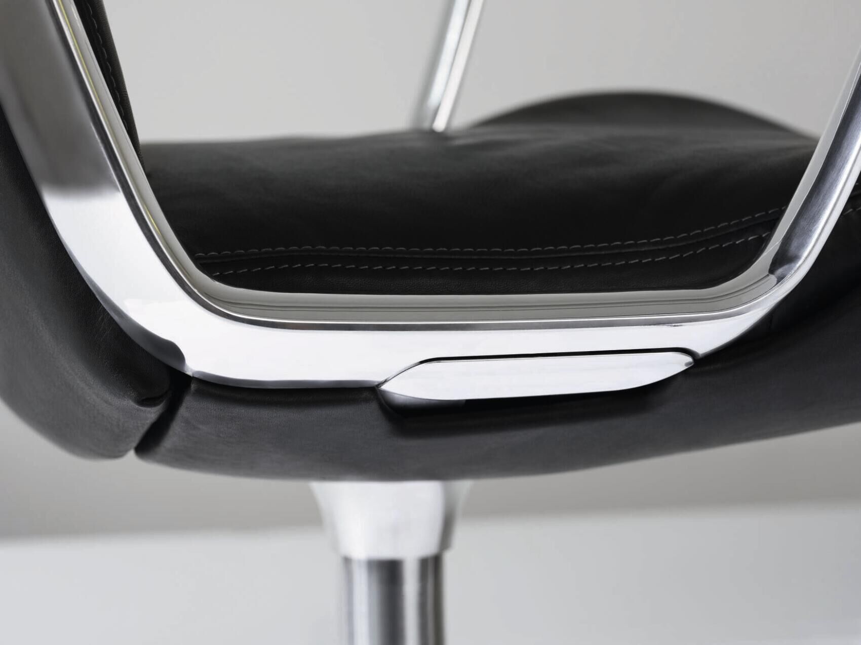 Nahaufnahme eines ergonomischen Bürostuhlsitzes mit verchromtem Rahmen und schwarzer Polsterung.
